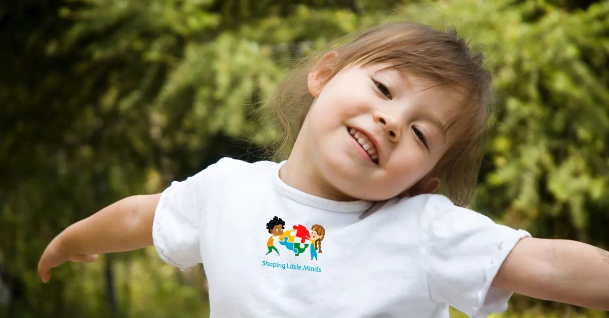 A child smiling outdoors in a Shaping Little Minds T-shirt